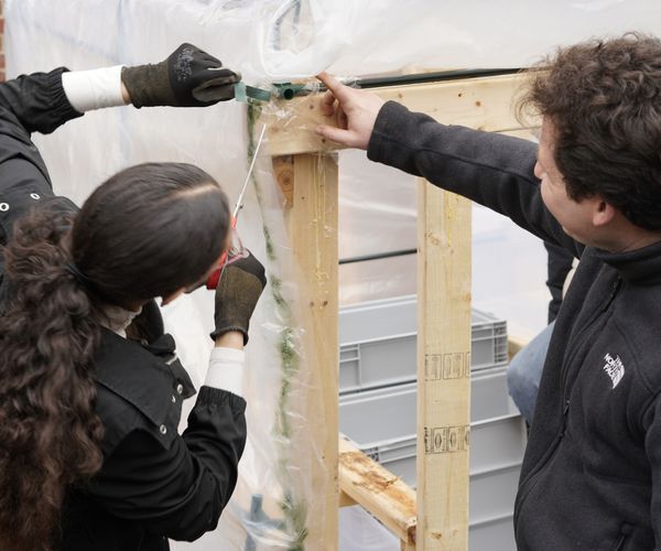 Two students measure a wooden frame.