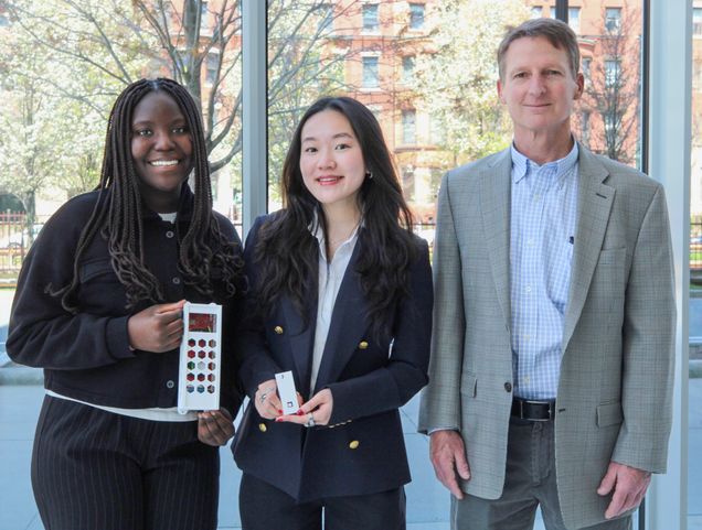 Two students with their faculty mentor hold an air quality monitor