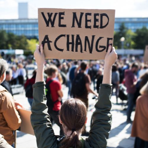 Person holding a sign at a protest that says "We Need a Change"