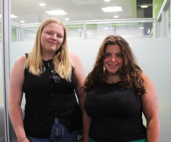 Two smiling students in an office space.