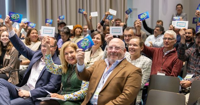 Audience holding up annual event artwork postcards.