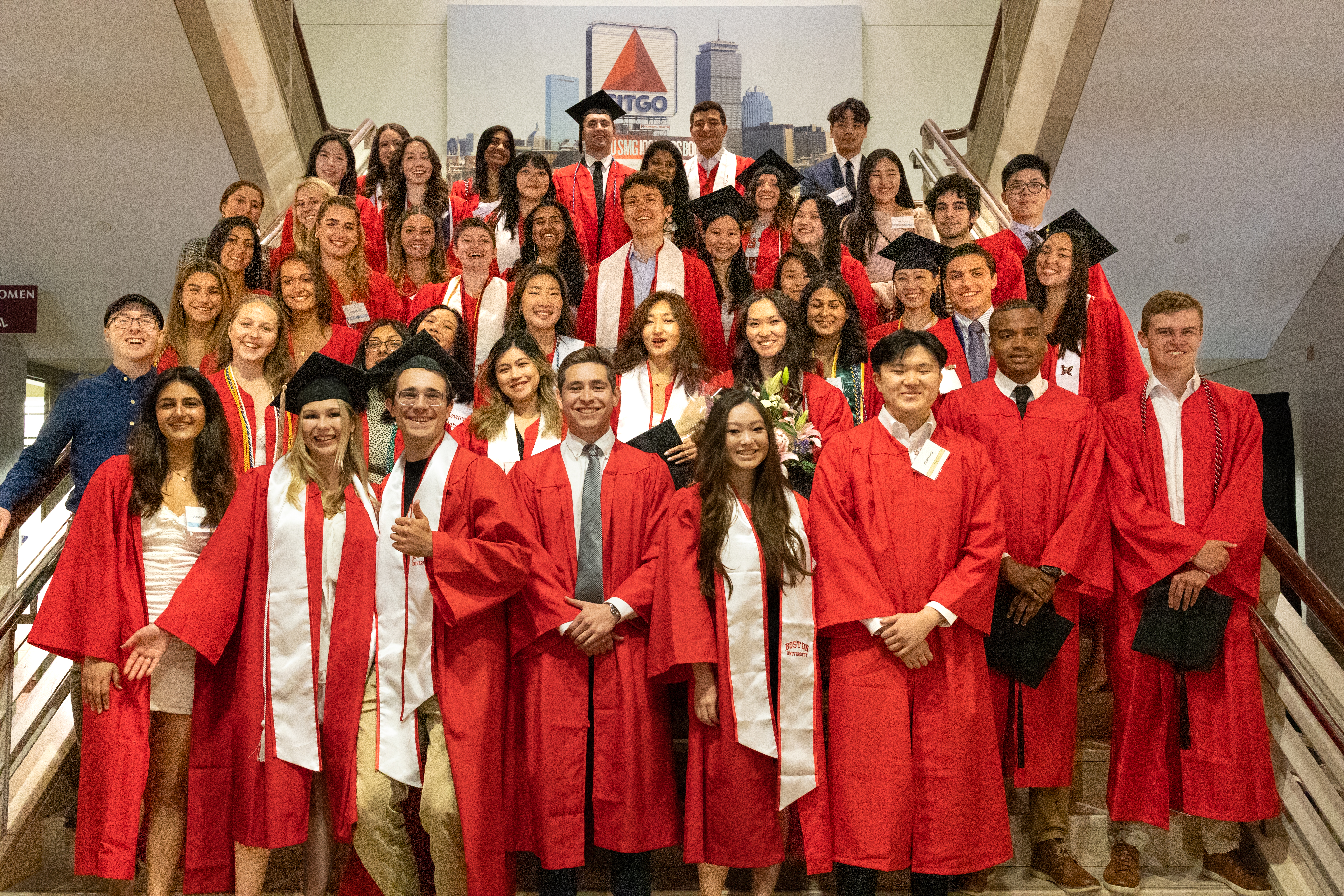 Large cohort of students in graduation gowns standing together in a stairwell