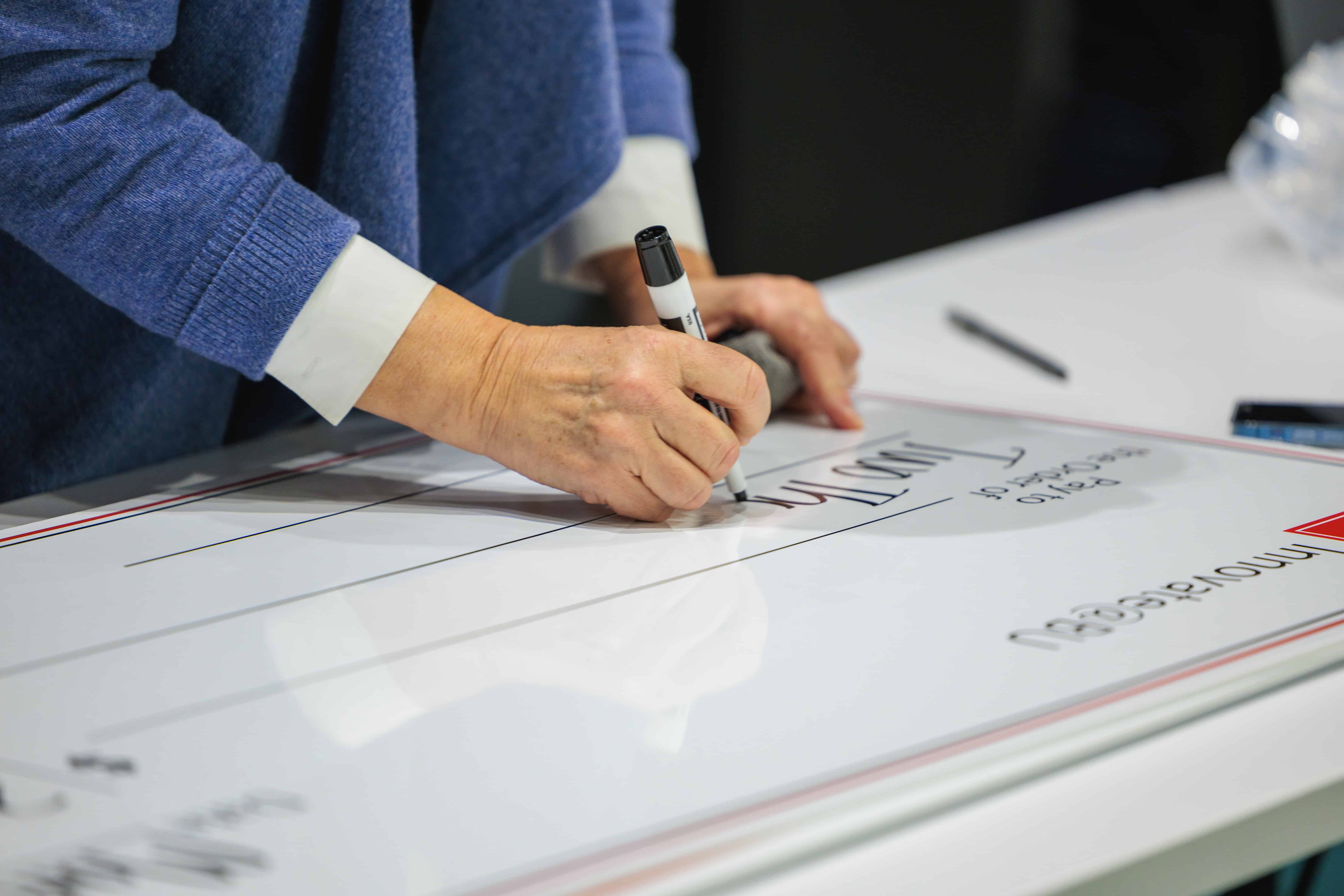A Woman's hand writing on a large check with an expo marker