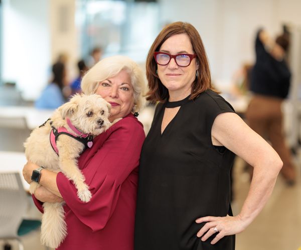 Two women pose for a photo while holding a small dog