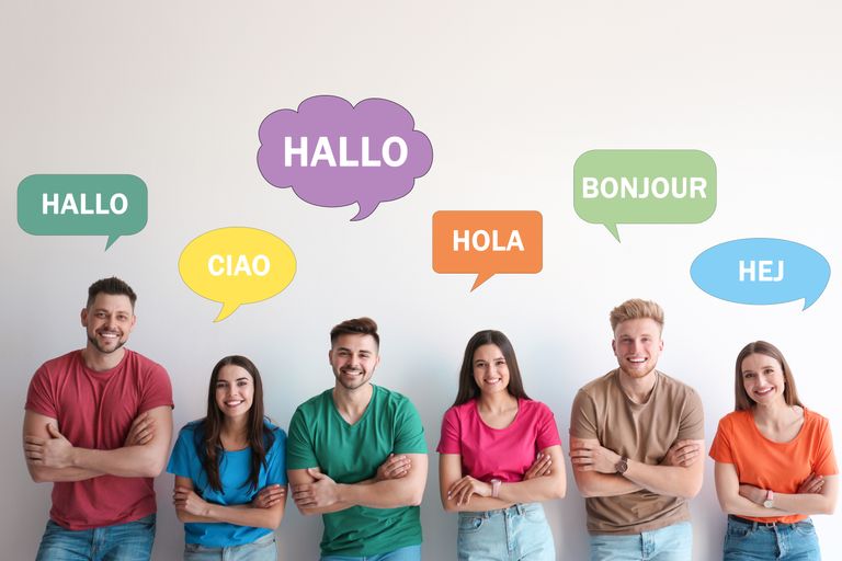 Happy people posing near light wall and illustration of speech bubbles with word Hello written in different languages
