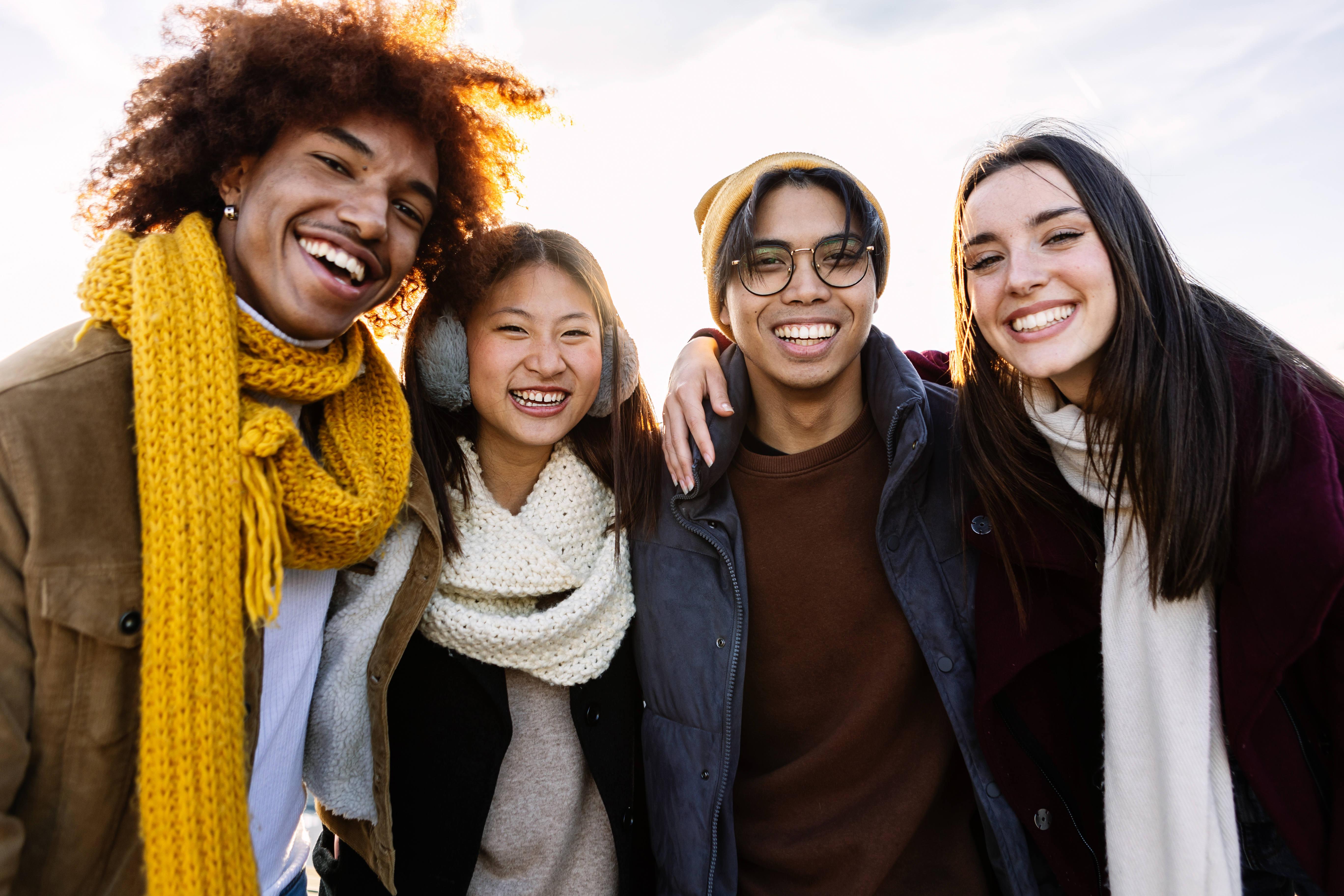 Portrait of four multiracial student friends in winter clothes smiling at cameraPortrait of four multiracial student friends in winter clothes smiling at camera