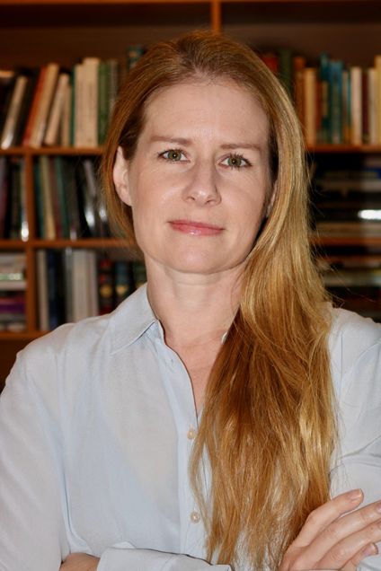 Picture of Erica Weiss, a white woman with long blond hair, looking at the camera with a bookshelf in the background.