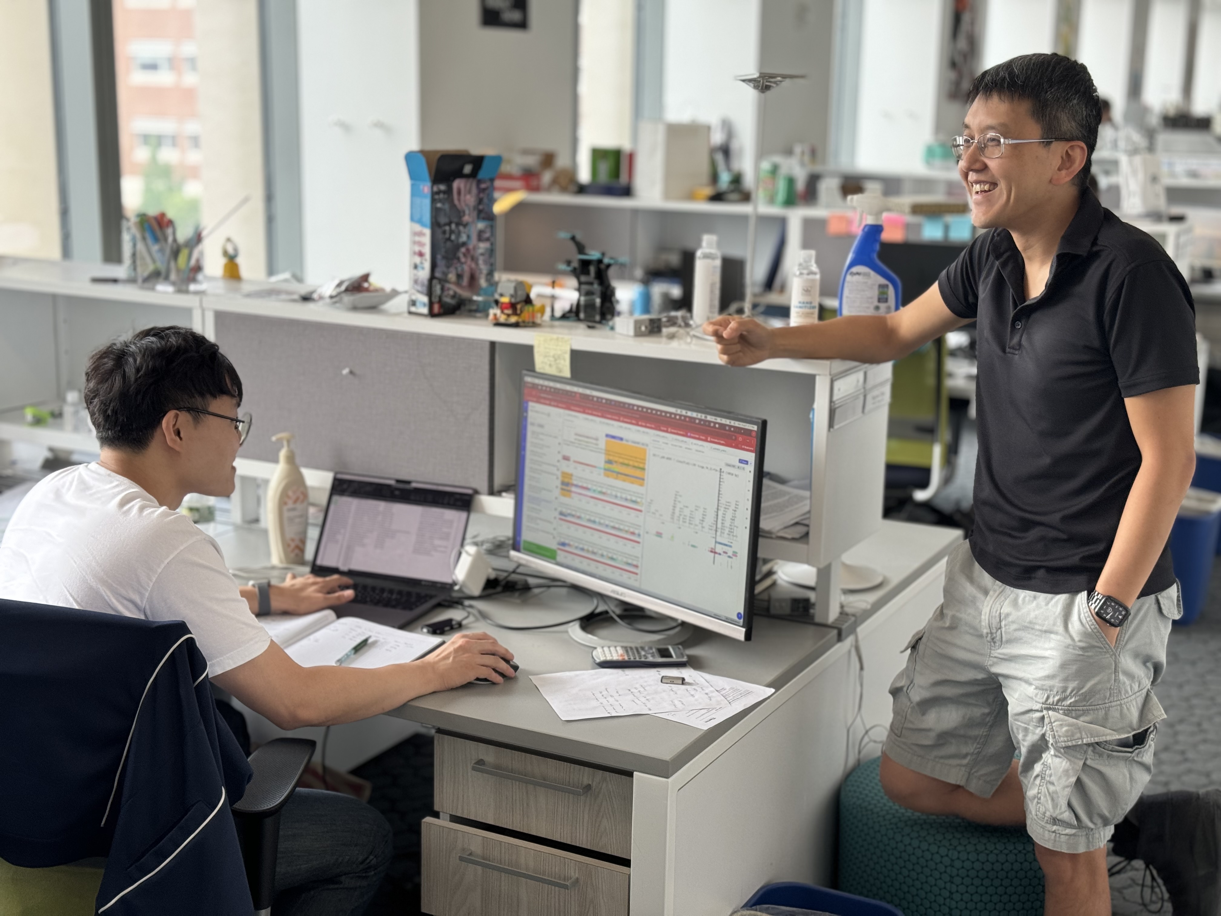 A man standing talking to another man seated at desk