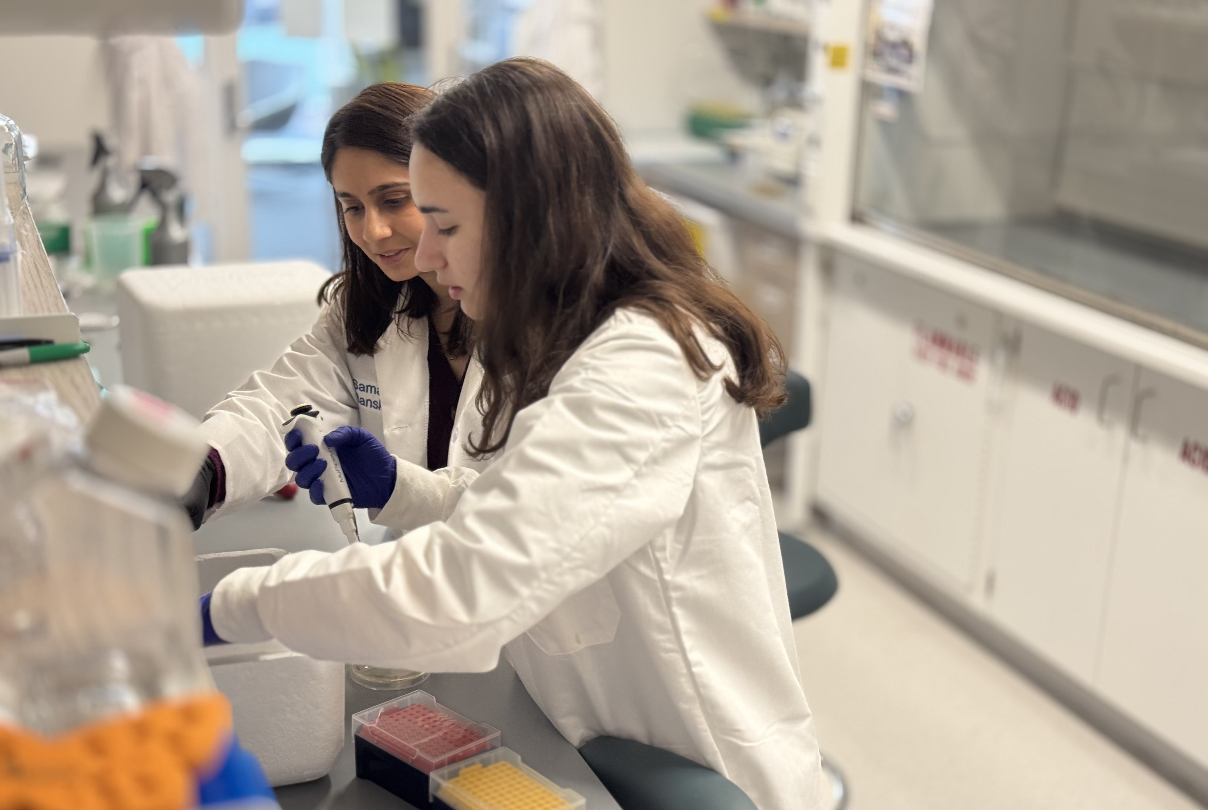 two people in lab coats pipetting in a wet lab
