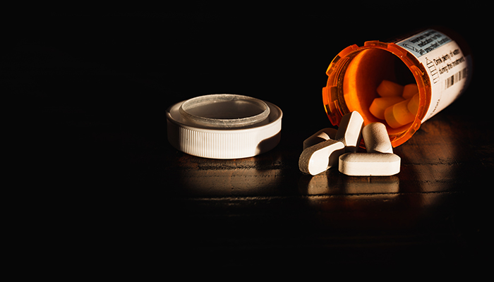 Close-up of prescription medication spilled outside of bottle onto a dark surface