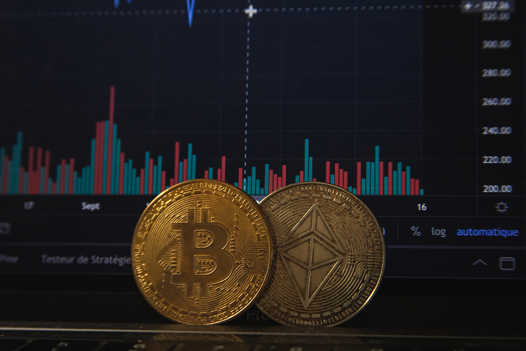 Two cryptocurrency coins in front of a computer screen with red and blue charts