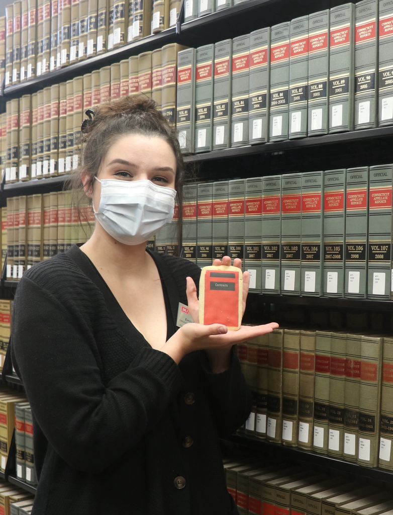 Woman holding a cookie decorated to look like a law casebook in the stacks at the BU Law library.