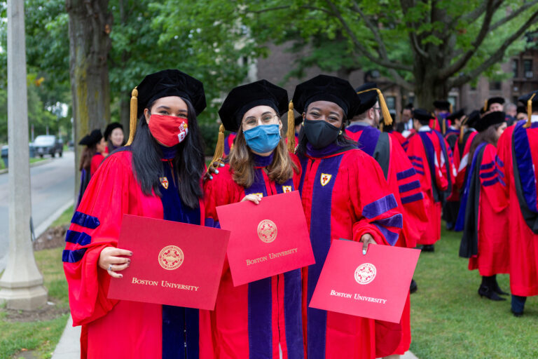 3 female BU Law graduates wearing regalia and displaying their BU Law degrees.