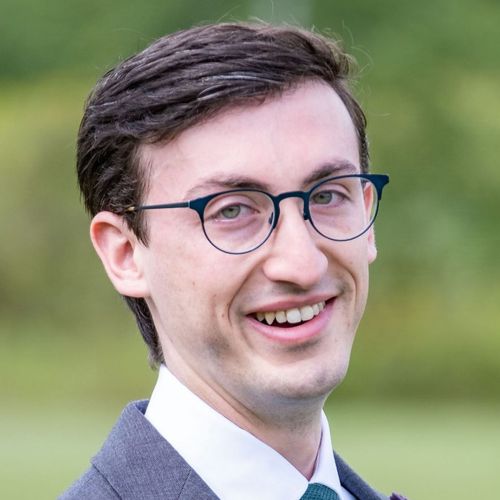 Portrait of Kevin Brown ('21) wearing glasses, jacket, and tie against natural background