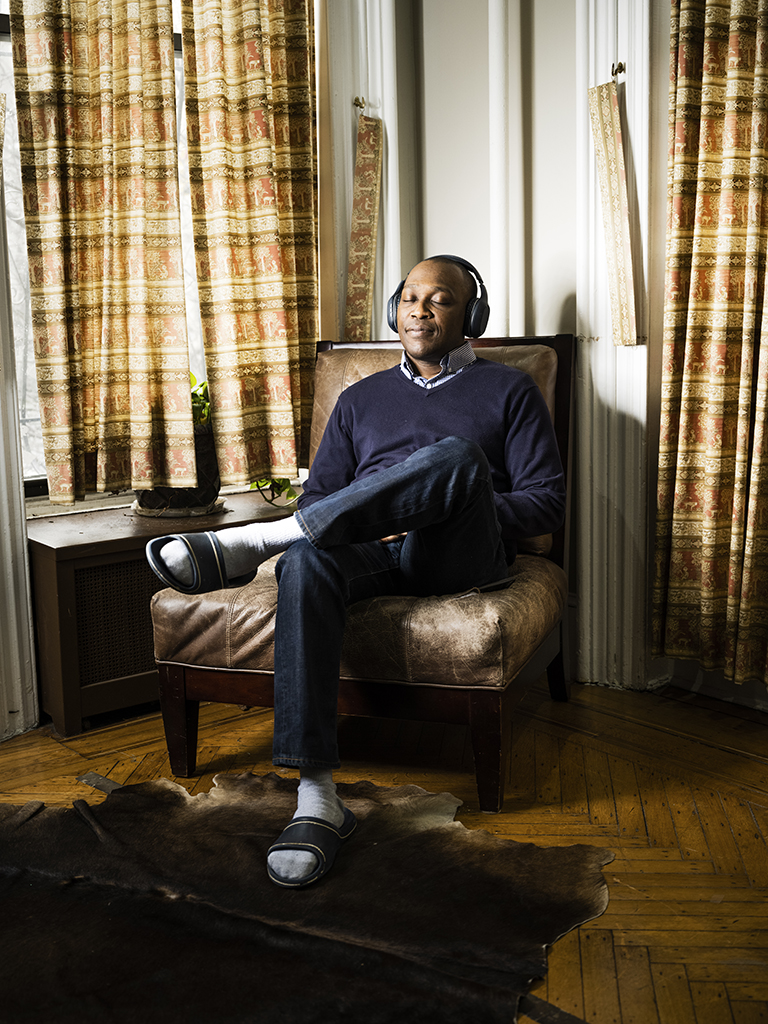 Jerry Juste sits in a leather chair with headphones on, eyes closed, legs crossed, listening to music