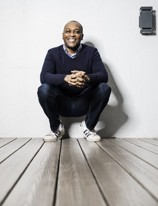 Jerry Juste kneels on his tiptoes against a white wall facing camera and smiling