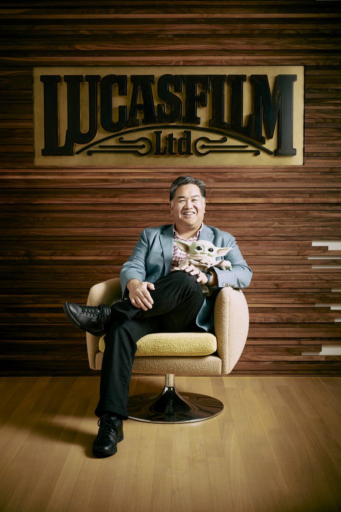 Ray Wu ('92) sitting in a chair beneath a Lucasfilm Ltd. sign and holding a baby Yoda doll.