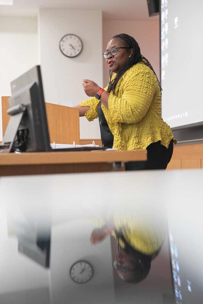 Dean Onwuachi-Willig lectures from the podium with computer screen in front.