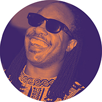 Orange duotone image of Stevie Wonder in sunglasses, smiling