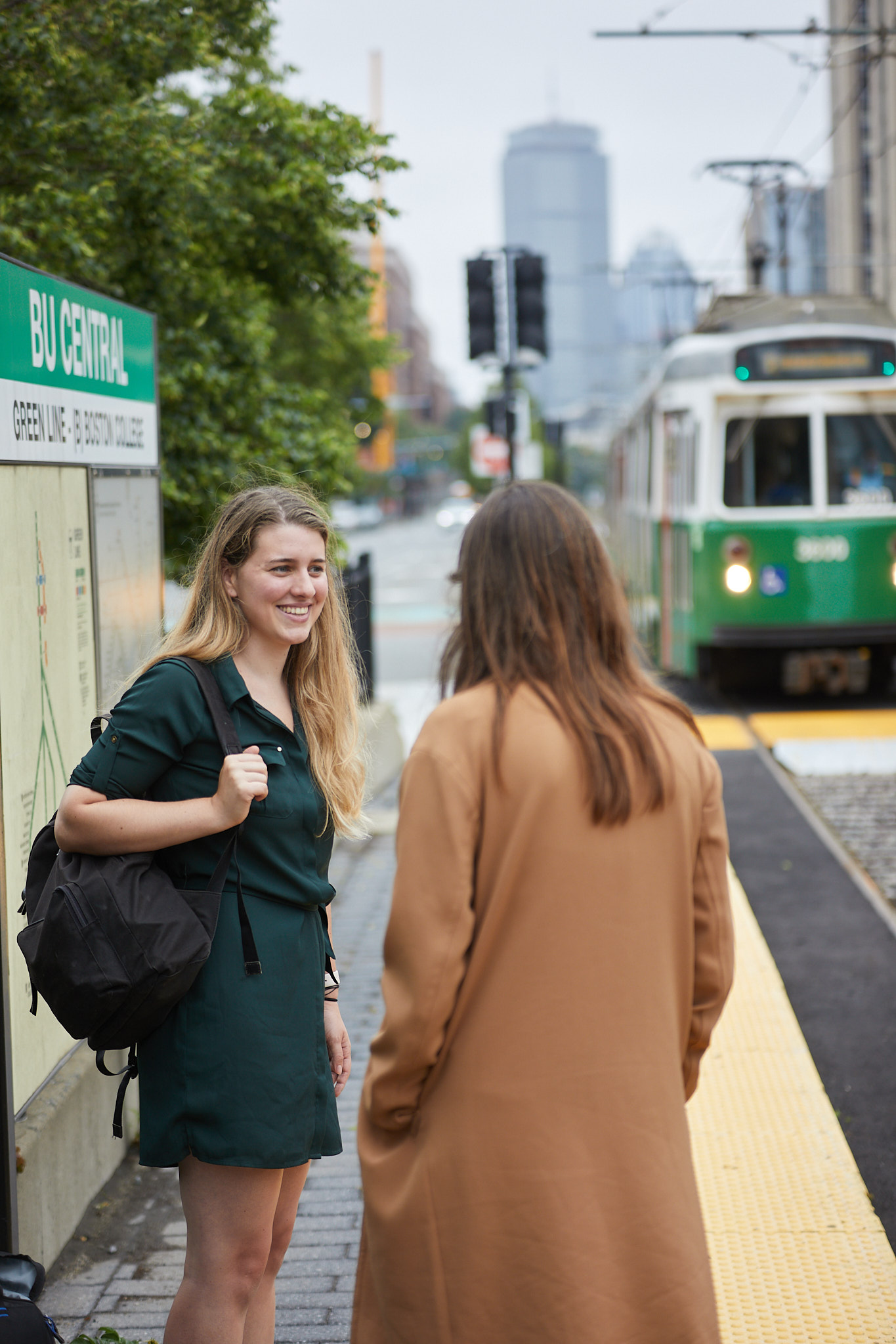 Two female students talking on comm ave waiting for the T as the green line approaches in the background