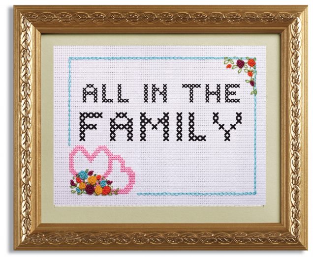 A framed cross stitch of the words "All in the Family"