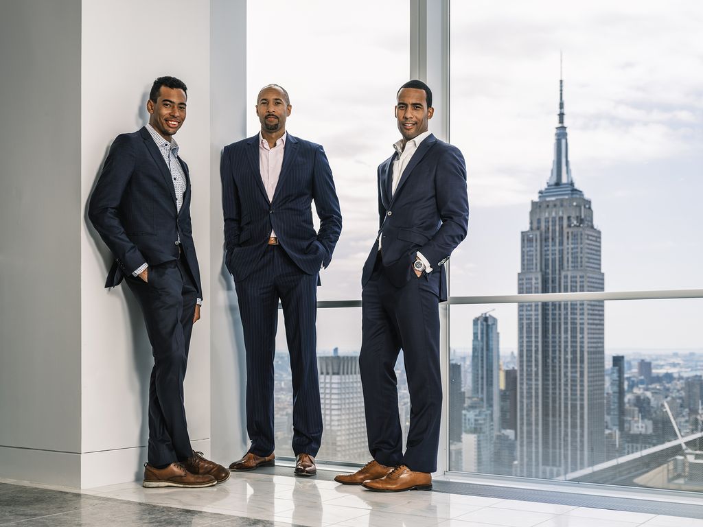 Timothy, Terence, and Trevor Rozier-Byrd stand in a high-rise in New York City with the Empire State Building in the background