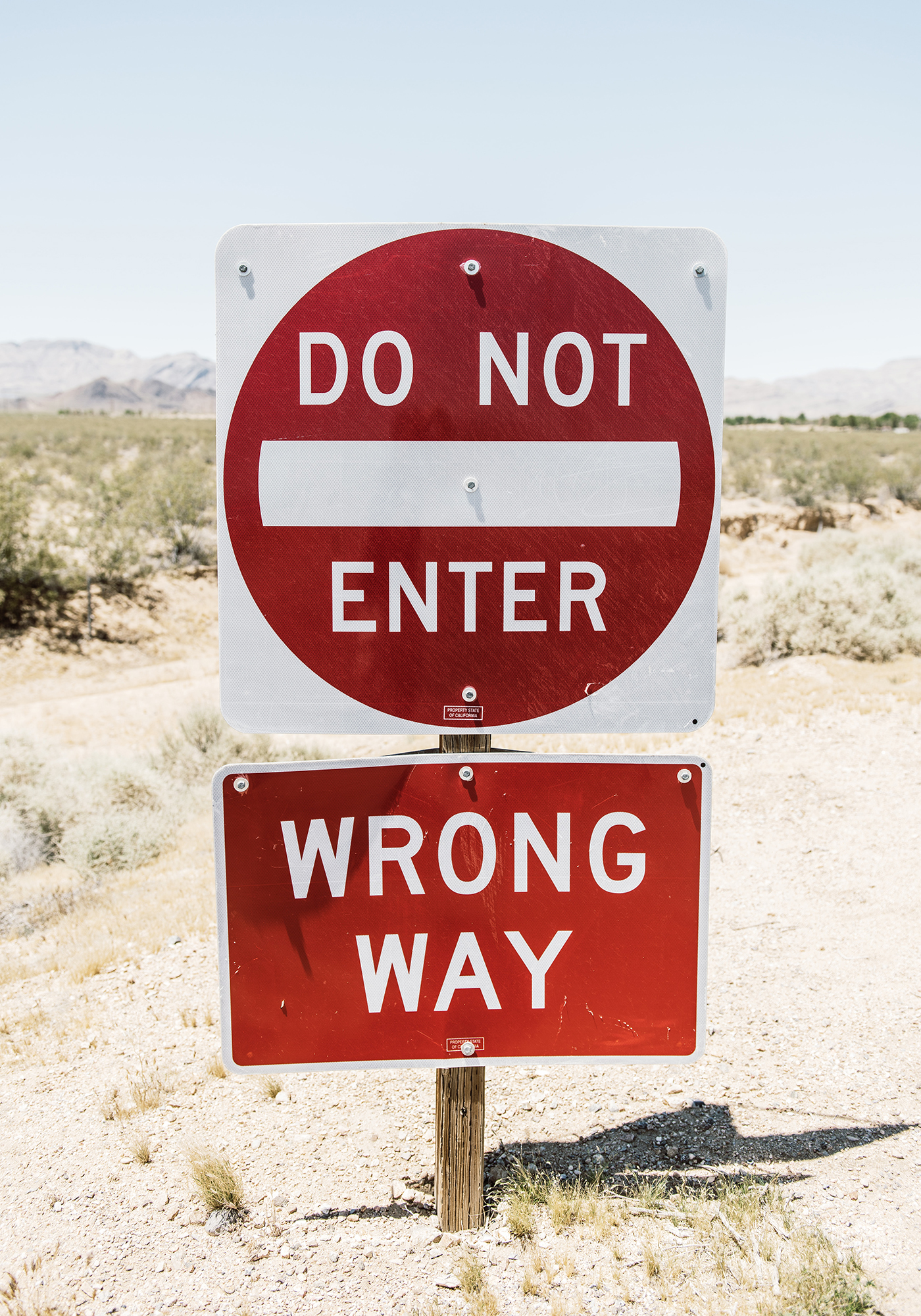Two road signs in the desert read Do Not Enter and Wrong Way