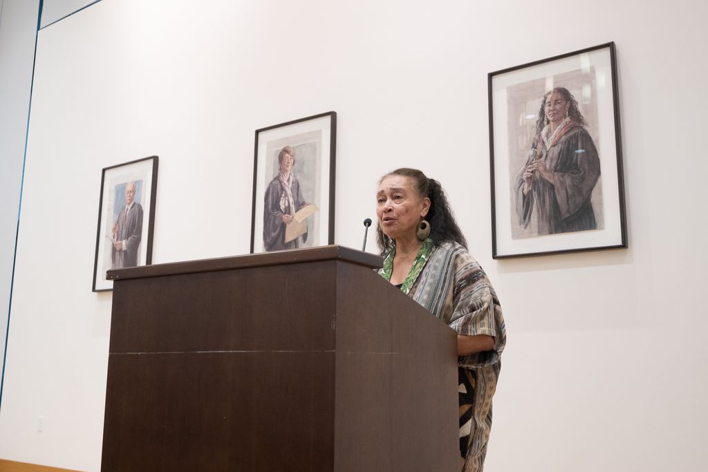 O. Rogeriee Thompson addresses the room from a podium in front of her portrait by Timothy J. Clark.