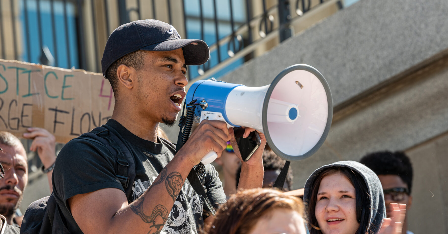 A young man speaks to a crowd through a bullhorn.