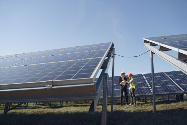 Two people stand in a field of large solar panels.
