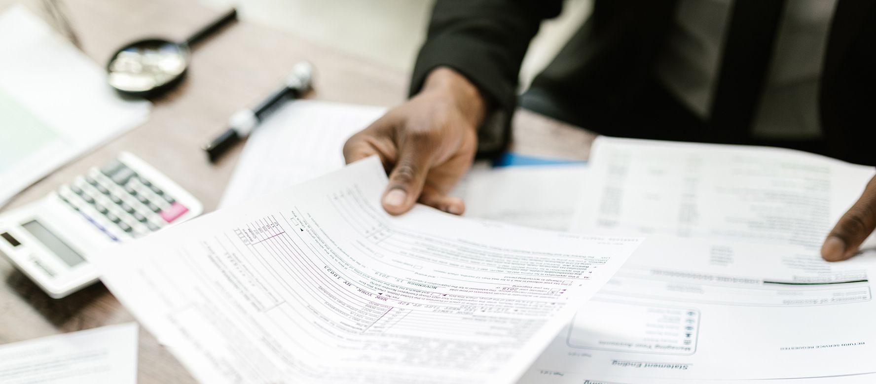 A closely cropped image of hands holding tax forms at a desk. There is a calculator on the desk.