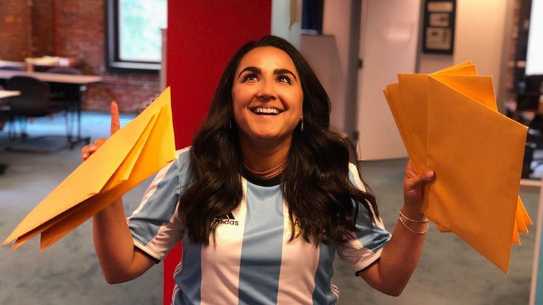 Jimena Mohedas in the Project Citizenship Offices holds manilla envelopes and points to the sky