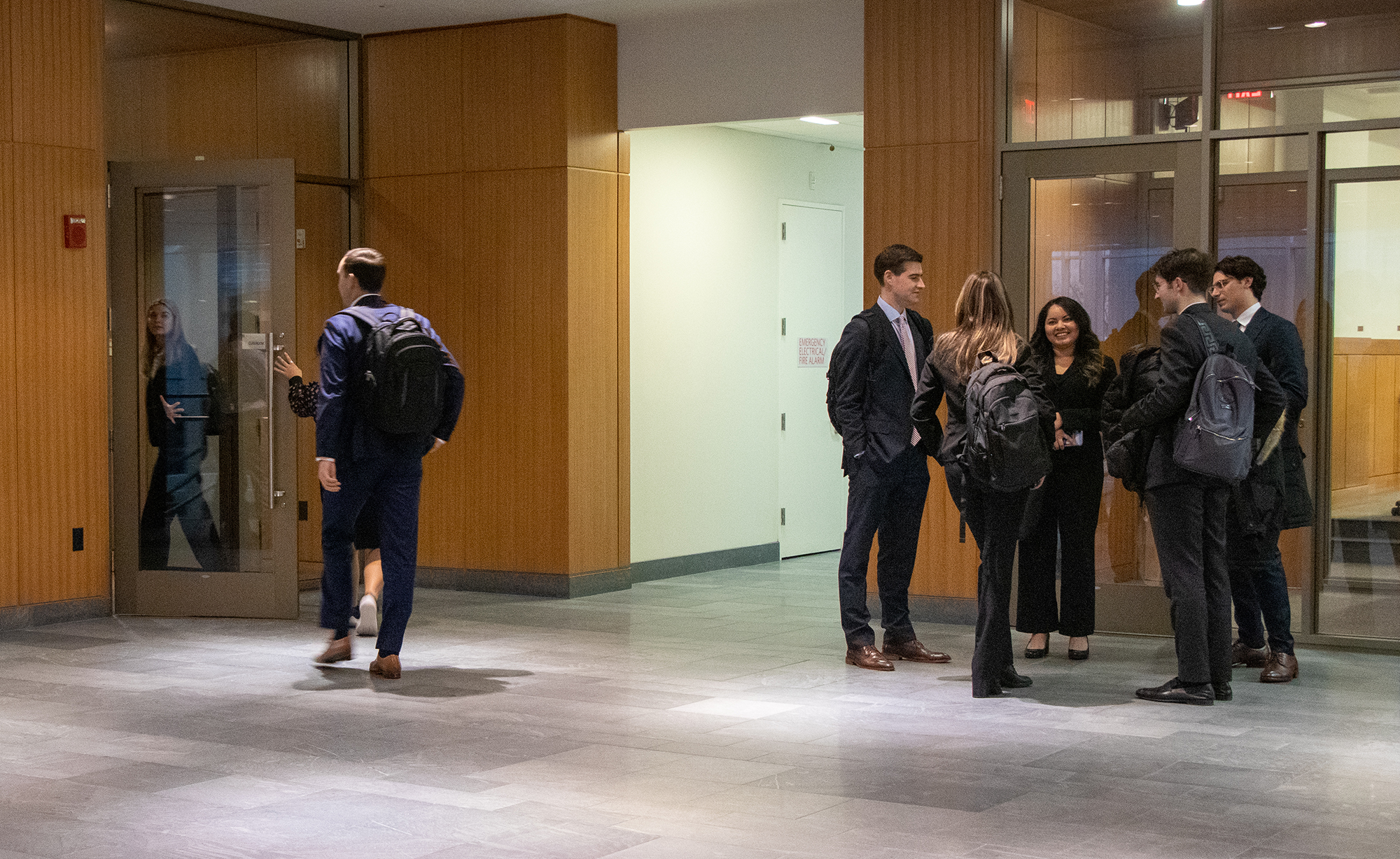 A group of students in business attire chat in the law tower atrium after a networking event.