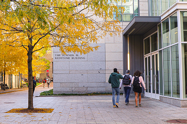 Three students walk outside the law complex on an autumn day.