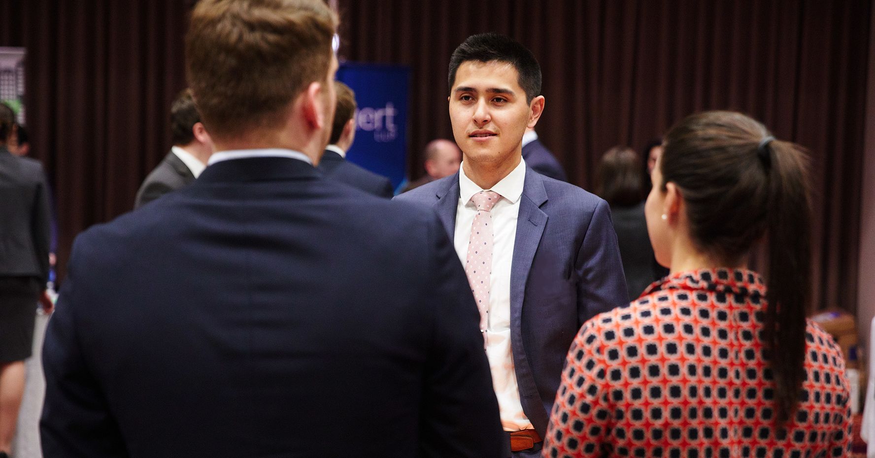 A BU Law student wearing a navy suit speaks with two people at a networking event.