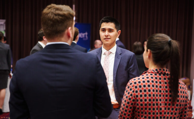 A BU Law student wearing a navy suit speaks with two people at a networking event.
