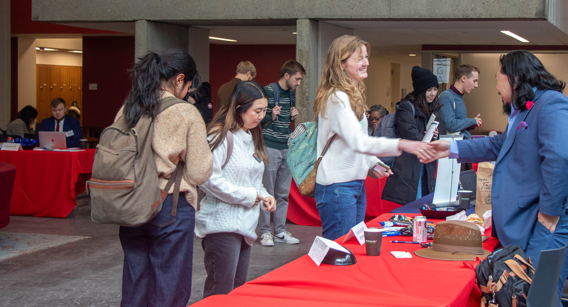 A student reaches across an event table to shake a recruiter's hand.