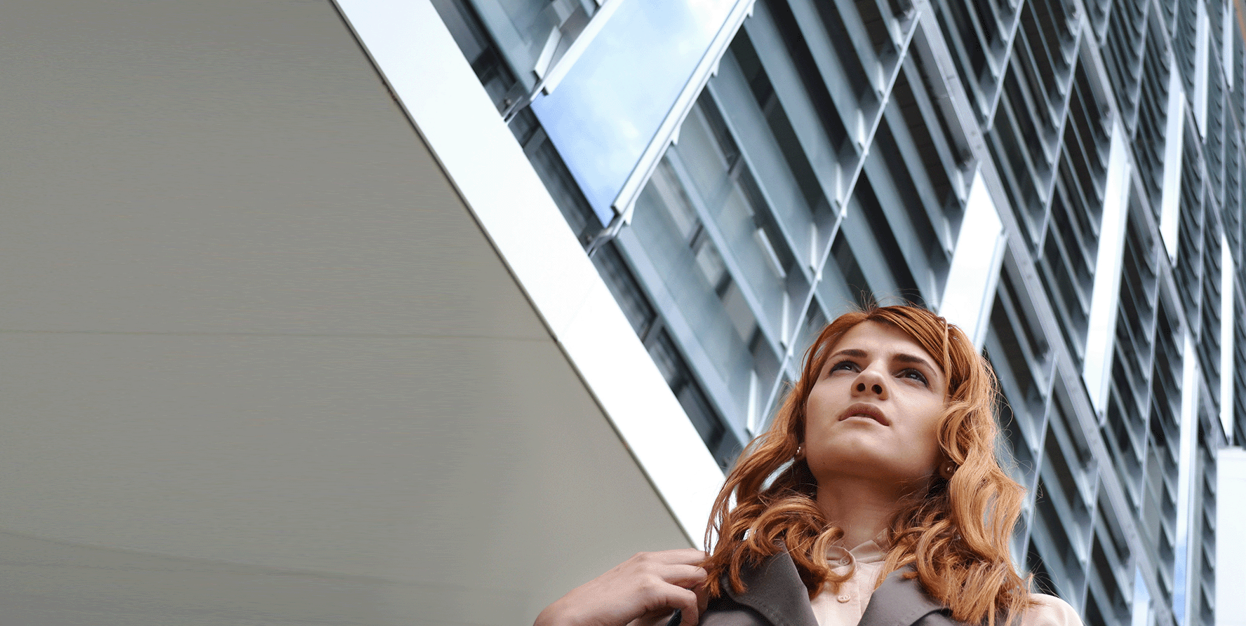 A woman in business attire walks outside. A skyscraper is in the background.