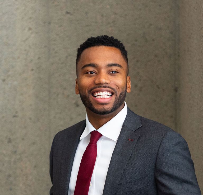 A smiling male student wears a gray suit and red tie.