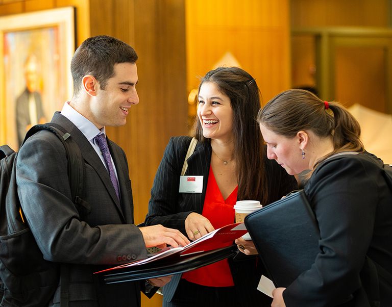 Three smiling students in business attire look at a folder together.