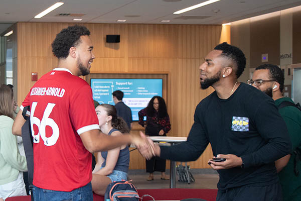 Two students shake hands in the atrium.