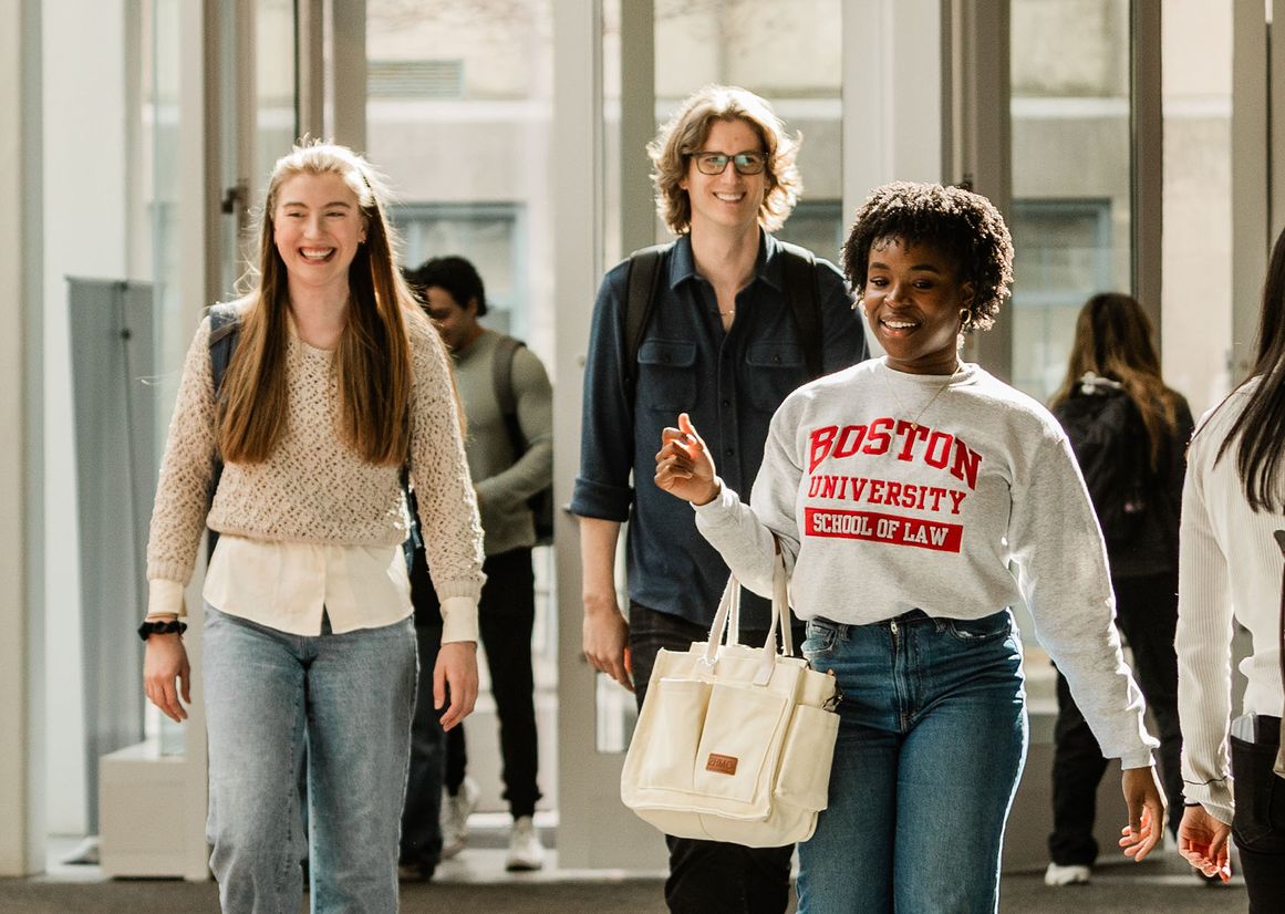 Three students smile as they walk through the front doors of the law tower.