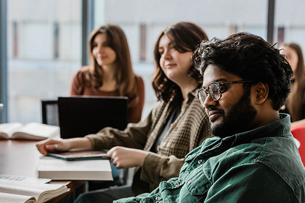 Students sit around a conference table and listen to a speaker.