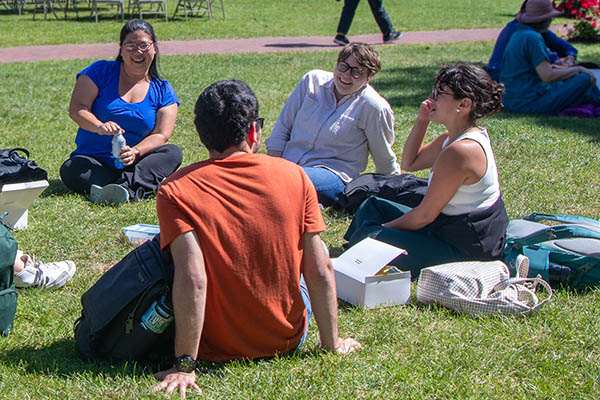 Students and BU Law staff sit on the grass outside the BU Law Complex in sunny weather.