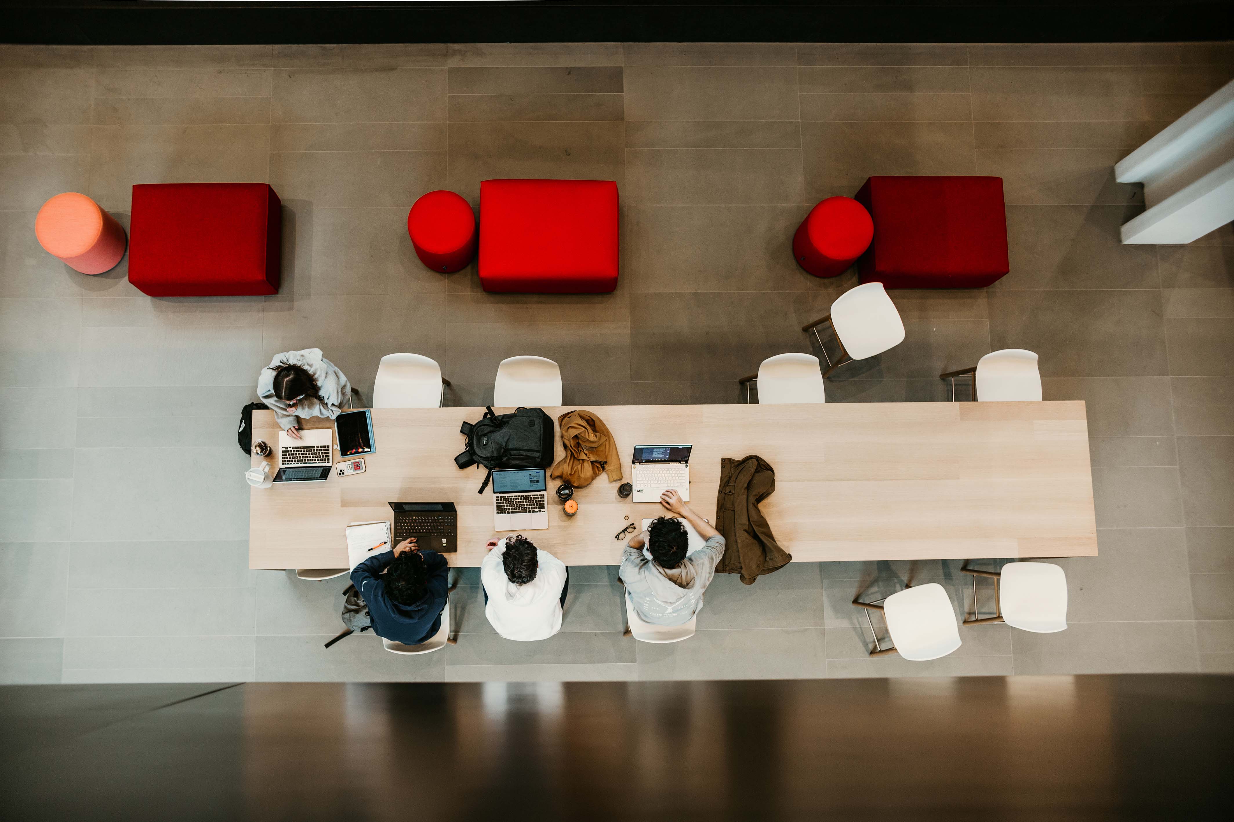 Image of three students sitting at a table with their laptops, taken from above them.