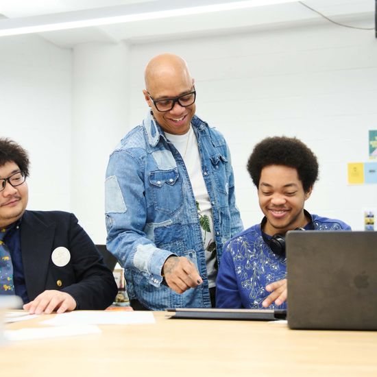 An instructor stands over two students who are sitting at a table with their tablets.