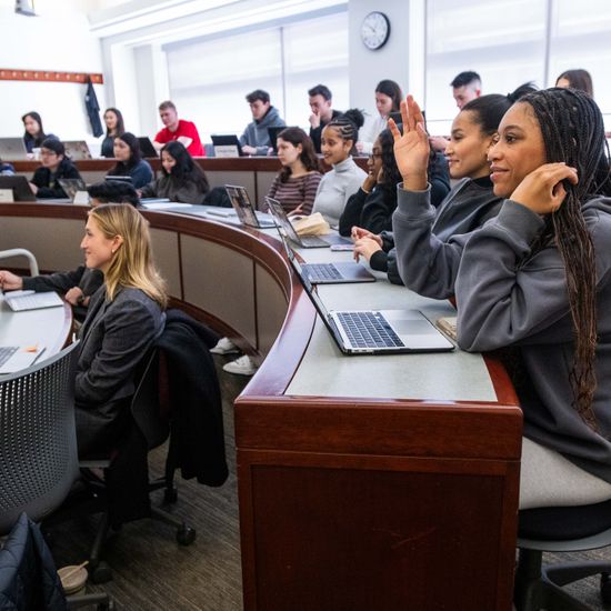 A student raises their hand in a full classroom