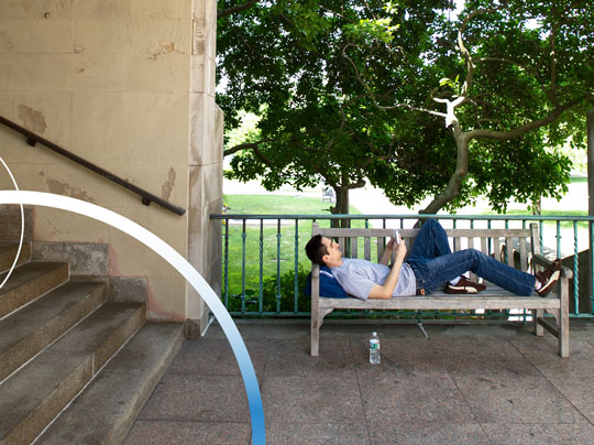 A Boston University student reclining and reading on a bench outdoors