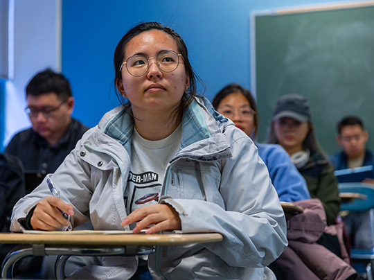 A BU MET Actuarial Science student seated at a desk in a classroom