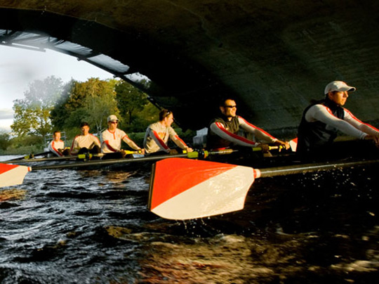 The BU men's rowing team crossing underneath a bridge on the Charles River